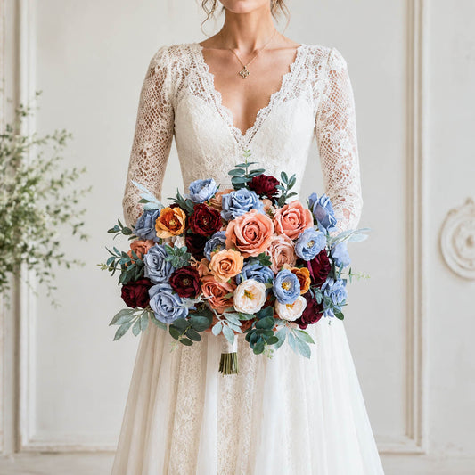 A bride in a white lace wedding dress holding a colorful bouquet of blue, orange, burgundy, and cream flowers, standing in a classic white interior with decorative wall molding.