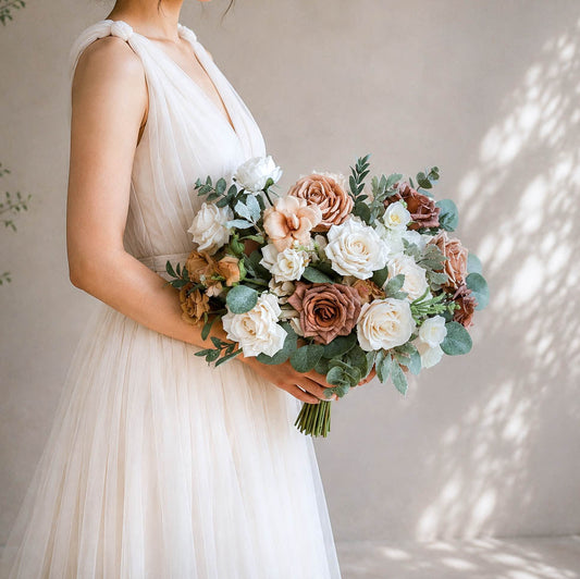 Bride holding a neutral artificial wedding bouquet with Quicksand and Toffee roses, ivory blooms, and soft greenery